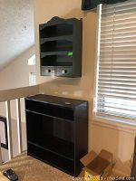 Photo showing both the decorative wall shelf installed on the wall and the small black bookcase on the floor beneath it.