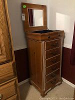 Front view of tall solid wood jewelry chest with hinged top mirror open, showing velvet lined compartment and six drawers.