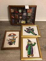 Four framed pieces displayed on the floor including glass shadowbox and clown embroidery prints.
