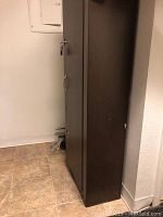 Full view of the tall brown metal gun safe positioned against a wall, showing size and condition.