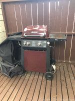 Full view of the maroon Brinkmann BBQ grill with attached side shelves and wheels, cover partially visible on left side