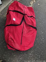 Red fabric storage bag for Christmas tree, fully zipped with black handles on asphalt floor