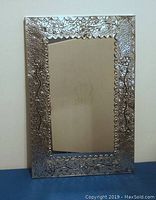 Front view of rectangular tin pressed mirror with floral embossed frame on white wall and blue surface