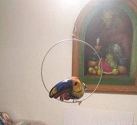 Side view of paper mache parrot hanging on circular metal hoop, showing vibrant colorful painted details of the parrot.