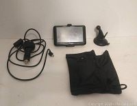 Image of Garmin GPS device with power cord, suction cup mount, and black protective pouch displayed on flat surface.
