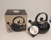 Photo of the boxed and unboxed black Copco tea kettle showing front and side with box and kettle together for reference.