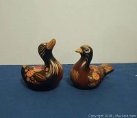Pair of two brown handmade Mexican duck figurines with floral design side by side on blue surface