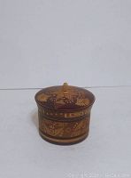 Closed small round wooden jewelry box with visible carved floral and geometric patterns on lid and body.