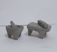 Front view of the two stone decor pieces: a small mortar with pestle and a metate with mano stone.