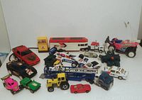 Overhead view of 15 toy cars and vehicles including race cars, trucks, and a toy bus on a white background.