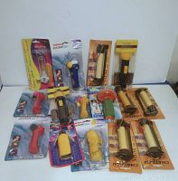 Photo showing 14 personal handheld fans in various colors and brands, all sealed in original packaging arranged on a flat surface against a white background.