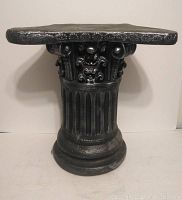 Front view of black plaster cast column with decorative capital and fluted shaft.