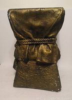 Front view of square plaster cast column showing textured gold finish, fabric draped design, and rope detail with some paint chipping.