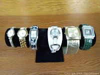 Six watches on black display stand, visible details of different bands and watch faces