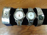 Four wristwatches placed on a black watch display roll, showing front and face detail of each watch from left to right.