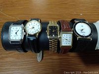 Five wrist watches arranged on display stand showing various face styles and bands.