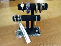 Full view of assorted jewellery on a black velvet display stand, showing watches, bracelets, chains, rings, and a packaged item.