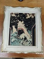 Front view of vintage framed coloured artwork showing a large shark with mouth open amid waves under dark sky