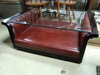 Angled view of the rectangular coffee table showing the glass top and padded red vinyl base with dark wood frame.