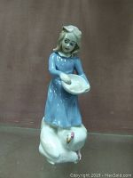Front view of Royal Doulton figurine depicting a girl in a blue dress holding a bowl while standing on a white hen.