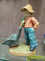 Front view of farm boy figurine holding green item interacting with goose