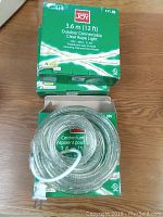 Three green boxes stacked containing 12 ft outdoor connectable clear rope lights coiled inside with visible plug.