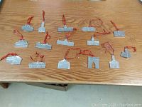 Overview of all 15 pewter collectible buildings arranged on a wooden table with red hanging loops visible on each piece.