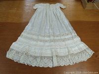 Full length photo of vintage child's christening gown laid out on wooden floor showing silk body and lace details