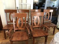 Front view of the 6 wooden chairs arranged in two rows, showing 4 armless chairs and 2 armchairs. Medium brown stain with oval cutout detail on backrests.