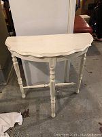 Photo of white painted demi lune table showing front and top surfaces along with turned legs and stretcher supporting structure.