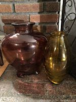 Two glass decorative vases side by side; one red and one gold, showing size and color differences