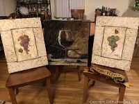 Four wine and grape themed decorative pieces shown on wooden chairs: two canvas grape pictures, one fabric tapestry with wine glass and grapes, and one resin plaque with text.