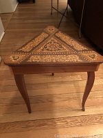 Photo of the triangular wooden table showing intricate floral and geometric inlaid patterns on the top surface with curved legs.
