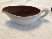 Side view of Stangl Pottery gravy boat showing brown interior and white exterior with handle and spout on towel surface.