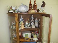 Cabinet with figurines inside on shelves and figurines, bookends, and snow globes on top shelf