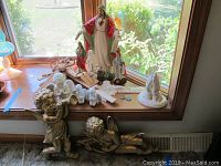Christian and angel figurines, coins, and wall art displayed on window sill and floor with natural light.