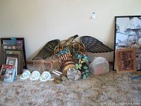 Wide view of wall art and decor items on carpet including eagle wings, metal butterflies, frames, plates, and wall hats.