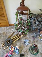 Birdcage-shaped ceiling hanging with faux plants, metal wind chimes, small baskets, and decorative items on carpeted floor near plants