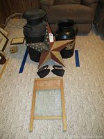 Two metal milk jugs, a wooden washboard with metal scrubbing surface, a decorative Americana star, and two vintage irons arranged on carpet.