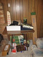 Overview of lot showing Albinar tripod box, projection screen box, lap desk, games and cards on a small table against wood panel wall