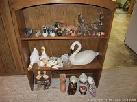 Wide view of wooden shelf with multiple shelves holding duck, swan, goose, rooster and shoe figurines in various sizes and types.