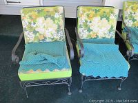 Two metal framed patio chairs with green floral patterned cushions and teal knitted covers on a porch surface.