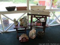 Full view of two wooden plant stands, multiple planters, and yard art including elephant figurine, children figurines, and birdhouse arranged in an enclosure.