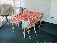 Photo of patio table and six matching chairs with table cloths on top. Table and chairs show weathering and rust, set on outdoor carpet.