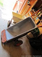 Metal Worx garden cart with orange handle and gray tub, Frank's yellow spreader behind, items placed on garage floor