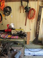 Various yard and garden tools arranged on shelves including hedge trimmer, blower, extension cords, and saws hung on the wall.