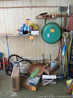 Wide view of the lot showing various cleaning supplies, wooden clothespins, brooms, mops, plastic wash tub, boxed appliances and other items.