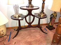 Full view of the vintage lyre base three level wooden table with lamps on top and nearby.