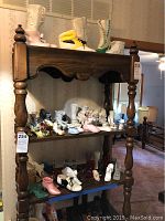 Photo of wooden shelf with multiple rows of ceramic and glass shoe figurines in various colors and styles.