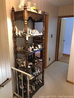 Front side view of wooden etagere with multiple shelves loaded with various small ceramic and glass decorative items.